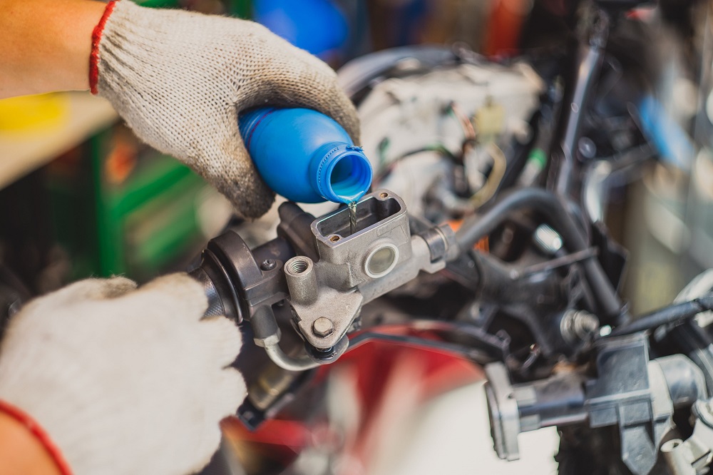 Mechanic checking and adding brake fluid on motorcycle brake reservoir in garage.