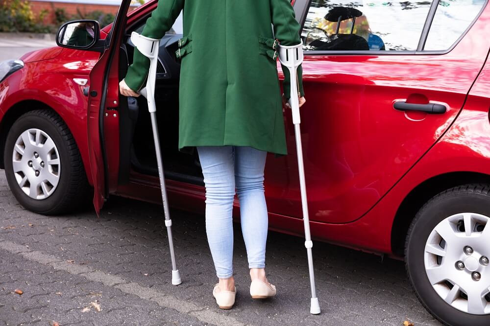 Woman on crutches getting inside the red car.