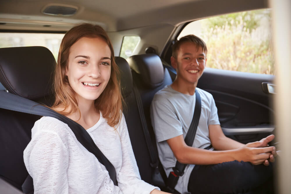 Girl and boy teens as backseat passengers wearing seatbelt for safety.