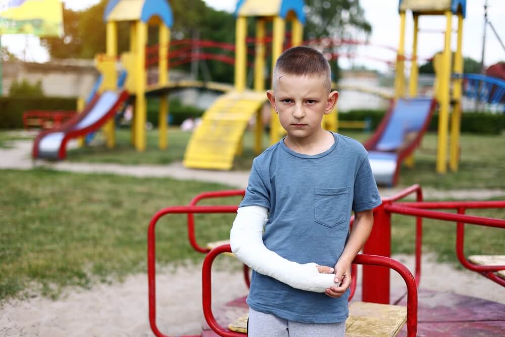 Unhappy kid with broken limb arm outdoors on playground.