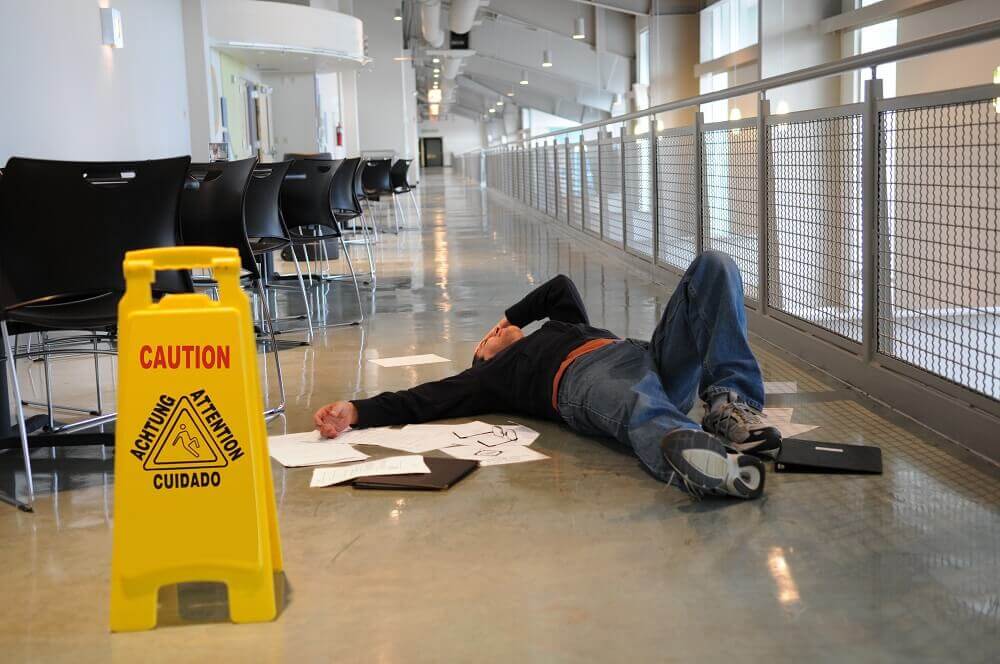 Employee slip and fall from slippery floor with caution sign.